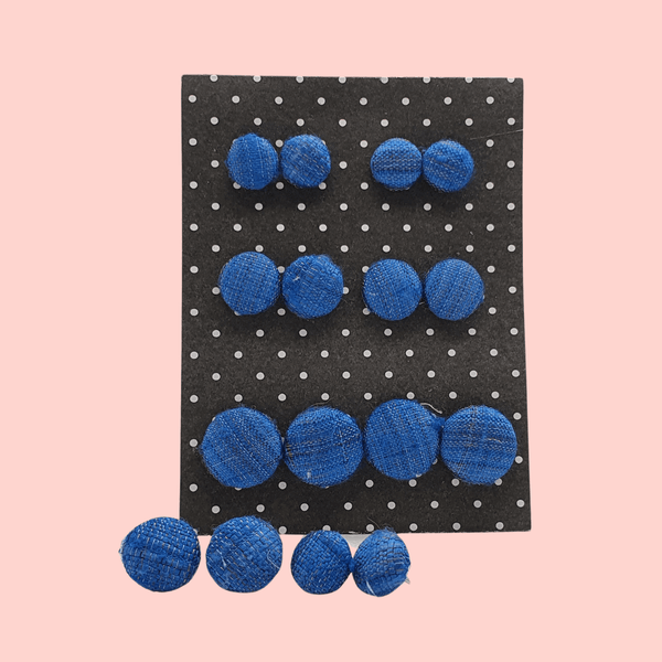 A black and white dotted diplay card showing off  8eight pairs of blue fabric button stud earrings