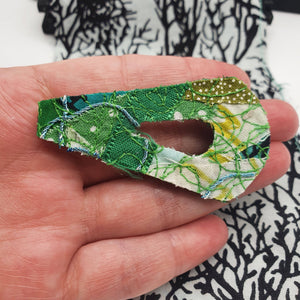 An 80's design fabric brooch made with a mixture of different shades of greens being held in a white woman's hand