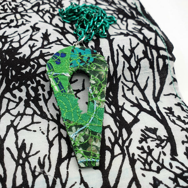 A green pendant on a green chain against a black and white background.