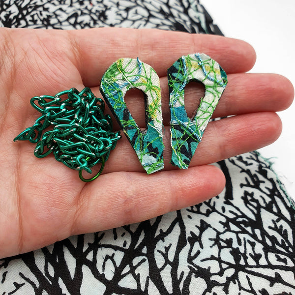 An 80's design fabric collar pin set made with a mixture of different shades of greens in a white woman's hand.