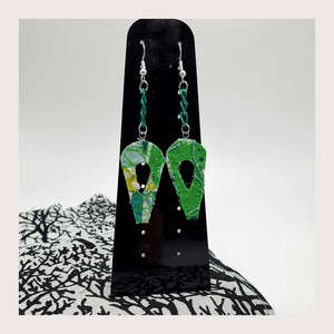 A pair of dangle style earrings hanging green chain displayed on a black acrylic stand.
