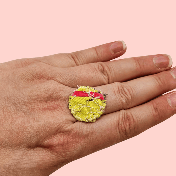 A circle fabric ring yellow fabric, a flash of pink ribbon across it and  yellow decorative stitching around the edge.
