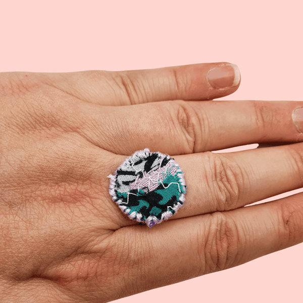 A circle fabric ring in green, pink and black fabric with lilac decorative stitching around the edge.